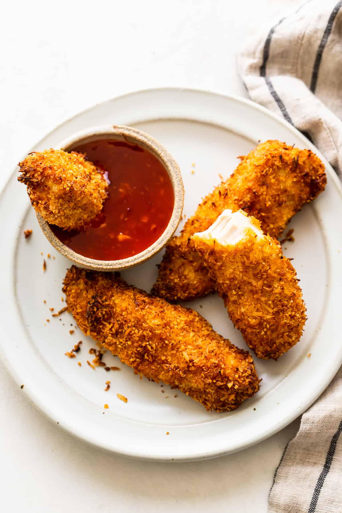 Crispy coconut chicken tenders on a plate with a dipping sauce.