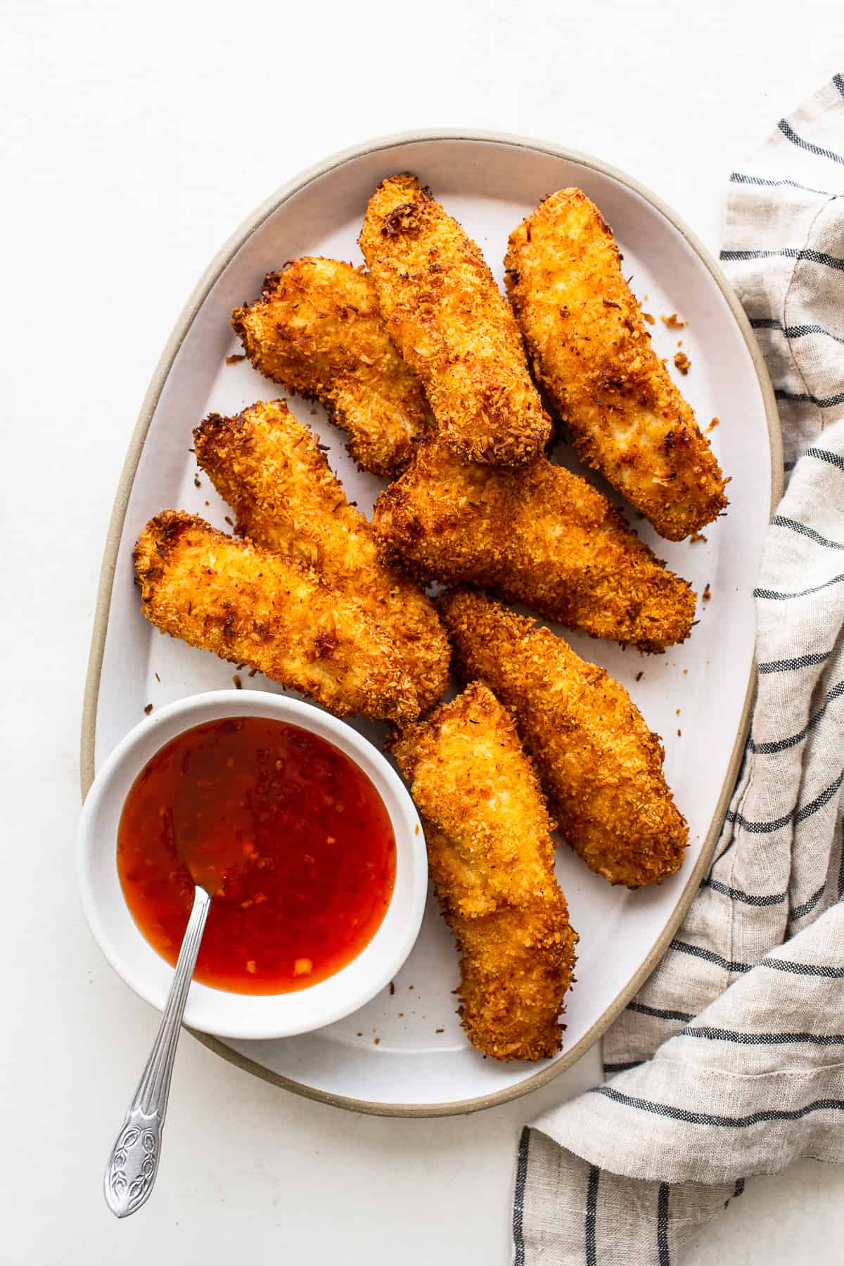 Air fryer coconut chicken tenders on a plate with sweet chili sauce.
