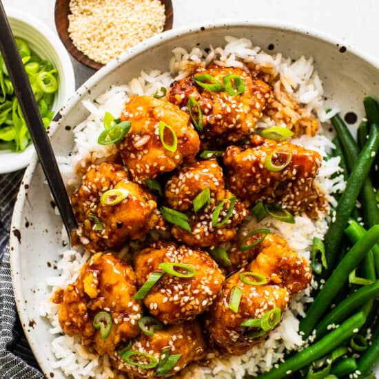 A bowl of sesame chicken with rice and green beans.