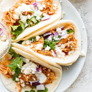 Three chicken tacos on a white plate.