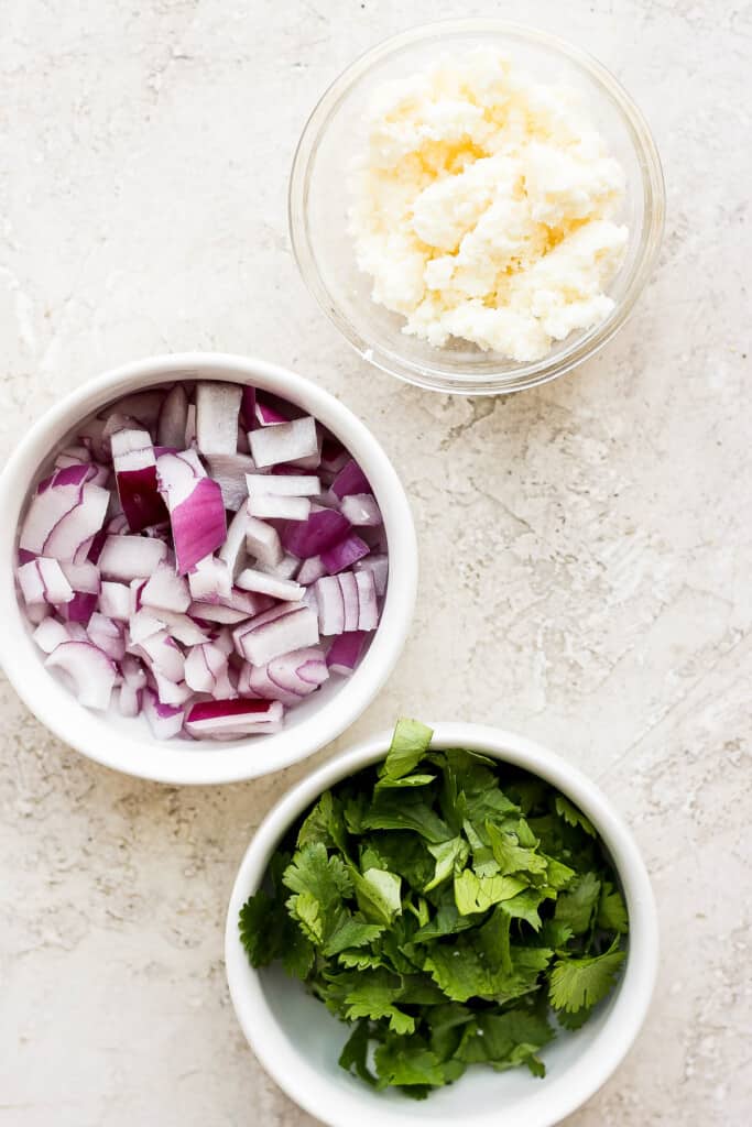 Red onion, cotija, and fresh cilantro in small bowls. 
