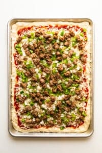 A pizza with meat and green peppers on a tray.