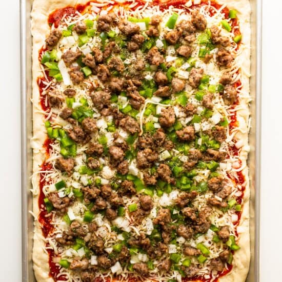 A pizza with meat and green peppers on a tray.