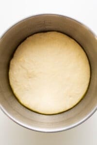 Dough in a metal bowl on a white surface.