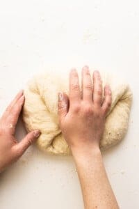 A person kneading a dough on a white surface.