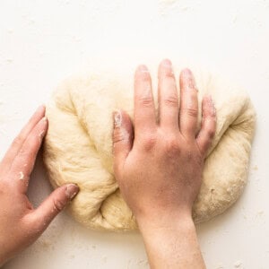 A person kneading a dough on a white surface.