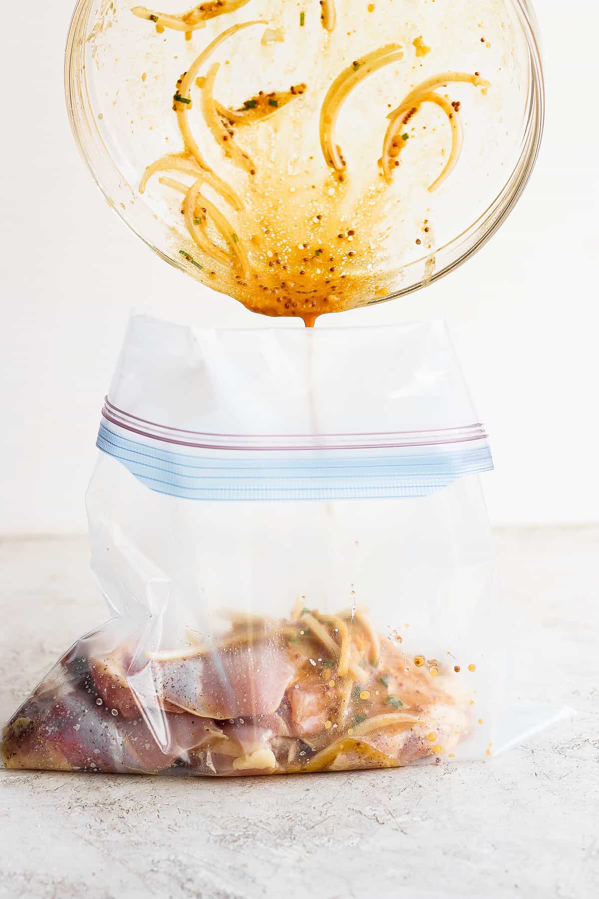 Chicken thighs marinade being poured in a gallon size bag.