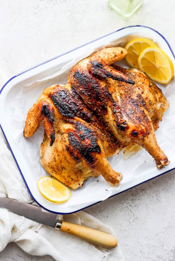 grilled whole chicken with lemon slices on platter.