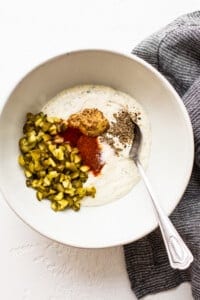 A bowl of yogurt with pickles and a spoon.