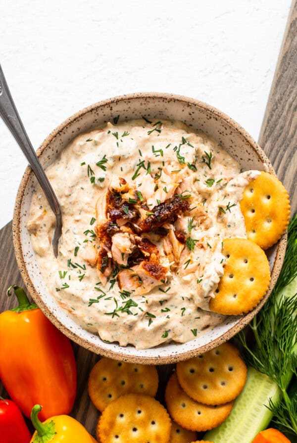 A bowl of smoked salmon dip with crackers and vegetables.