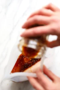 A person pouring homemade teriyaki sauce into a plastic bag.