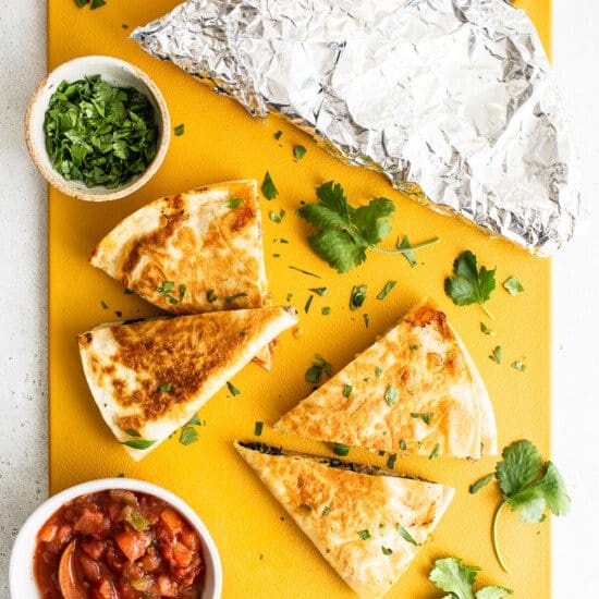 Quesadillas and guacamole on a yellow cutting board.