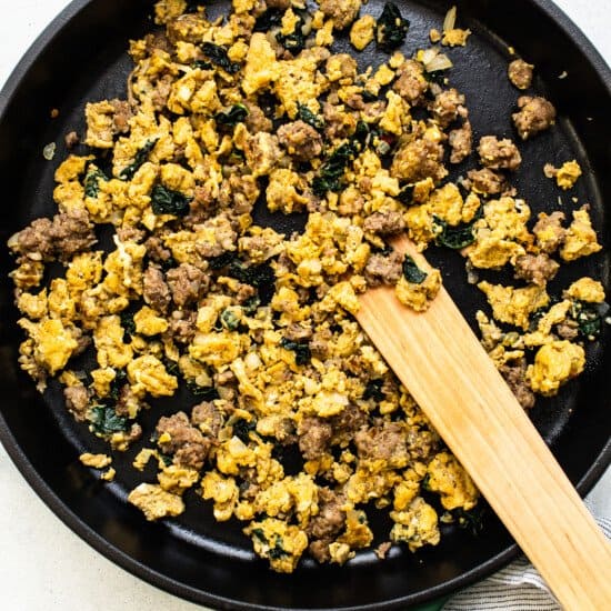 Scrambled eggs in a skillet with a wooden spatula.