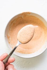 A person holding a spoon full of a brown sauce in a bowl.