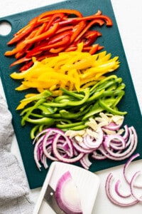 Sliced peppers and onions on a cutting board.