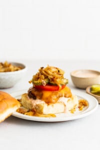 A homemade burger with onions and pickles on a plate.