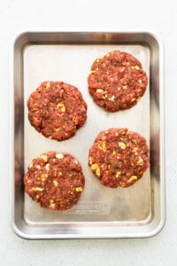 Four beef burgers on a baking sheet.