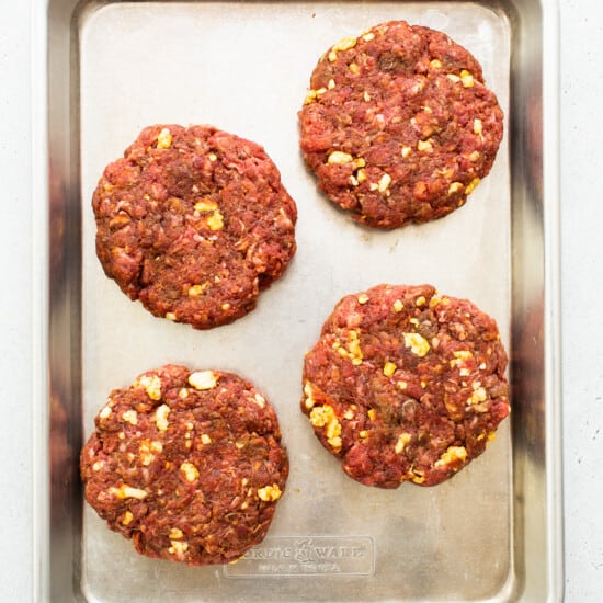 Four beef burgers on a baking sheet.