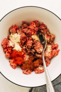 A bowl of meat and spices with a spoon.