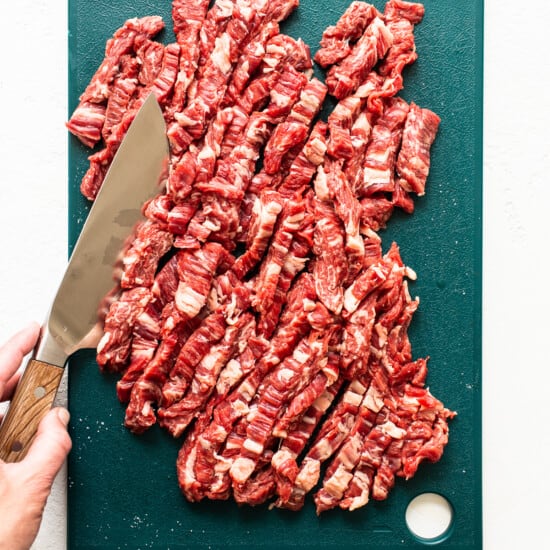 A person cutting a piece of beef on a cutting board.