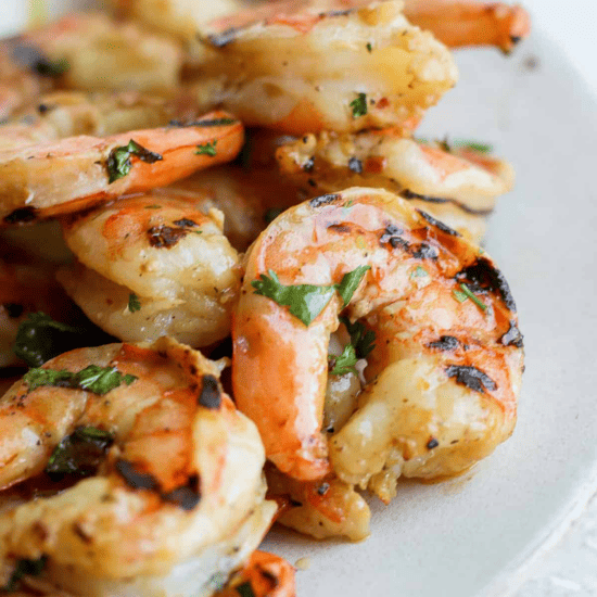 Grilled shrimp on a plate with lemon wedges, marinated.