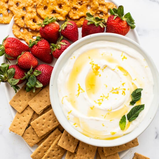 A bowl of dip with strawberries and crackers on a white plate.