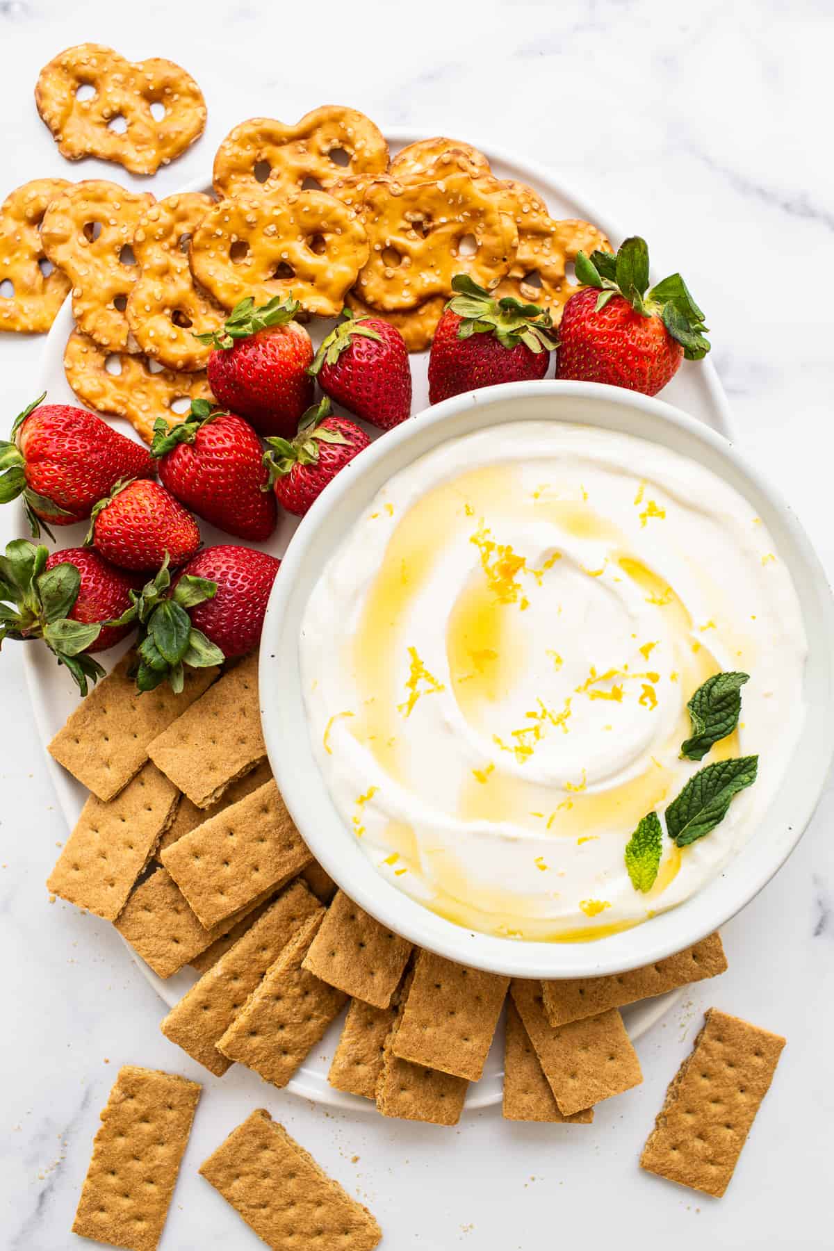 Bowl of fruit dip surrounded by berries, pretzels and graham crackers.