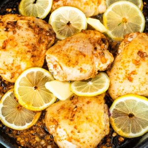 Chicken in a skillet with lemon slices.