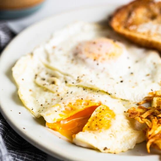 A plate with a fried egg, potatoes and a jar of peanut butter.