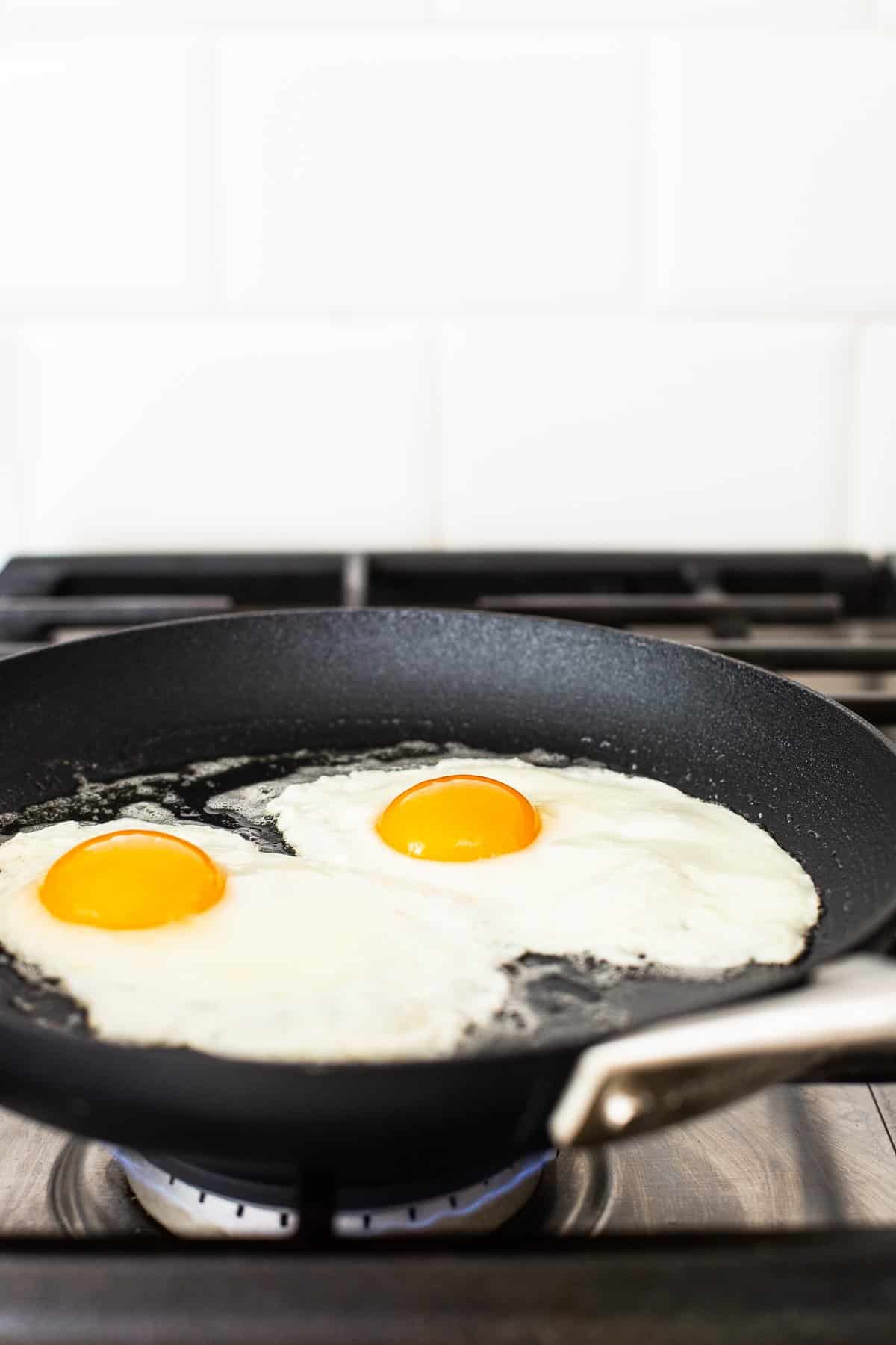 Eggs frying in a skillet to over medium.