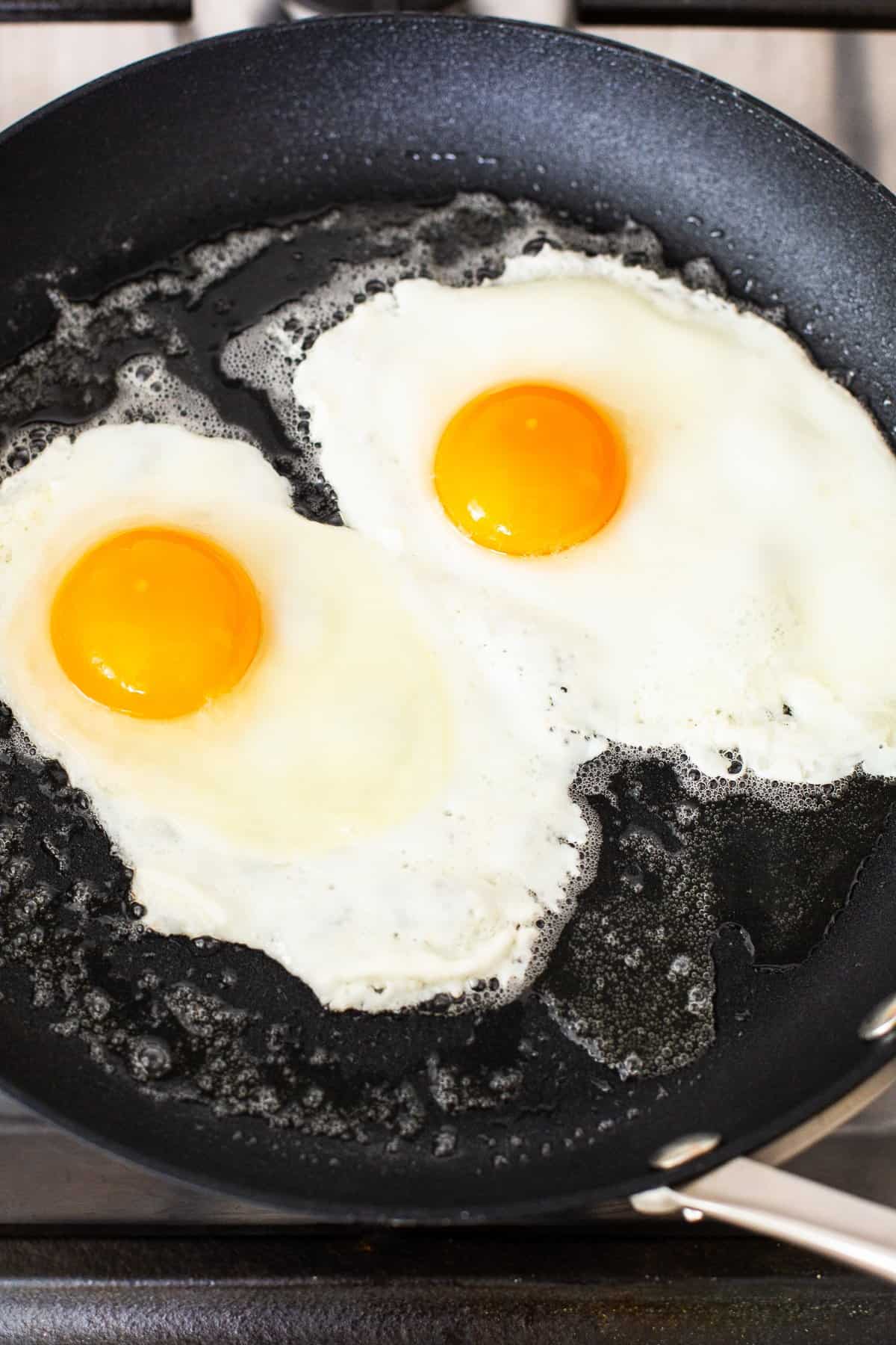 Eggs frying in a skillet to over medium.