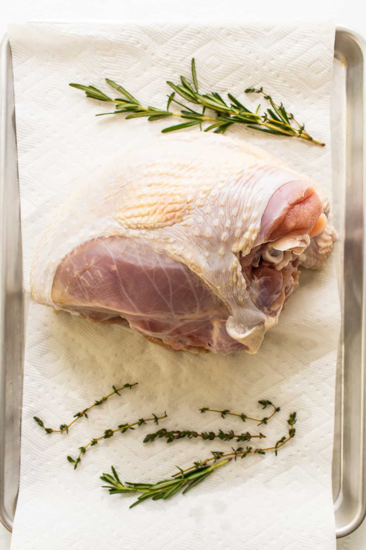 A turkey breast on a paper towel and fresh herbs. 