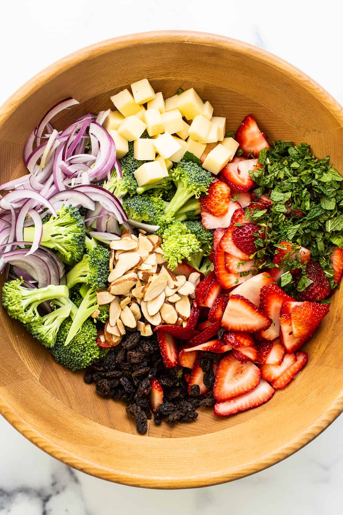 Ingredients for strawberry broccoli salad in a large wooden bowl.