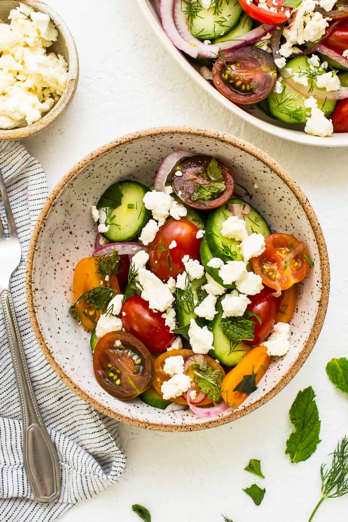 A bowl of cucumbers tomato salad topped with feta. 