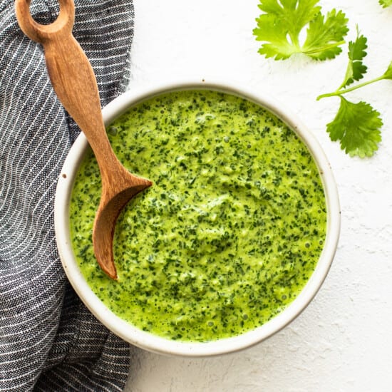 A bowl of green sauce with a wooden spoon.