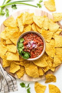 Nachos with salsa on a wooden cutting board.