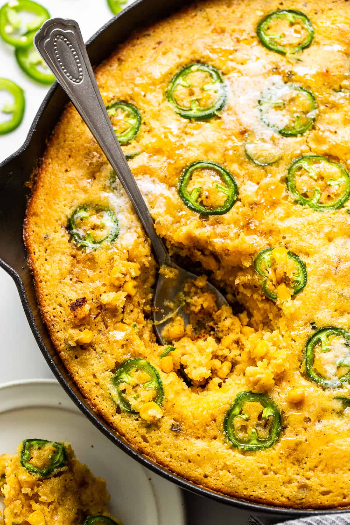 A spoon scooped into a skillet or jalapeno corn pudding.