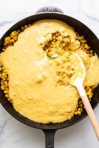 Corn on the cob in a skillet with a wooden spoon.