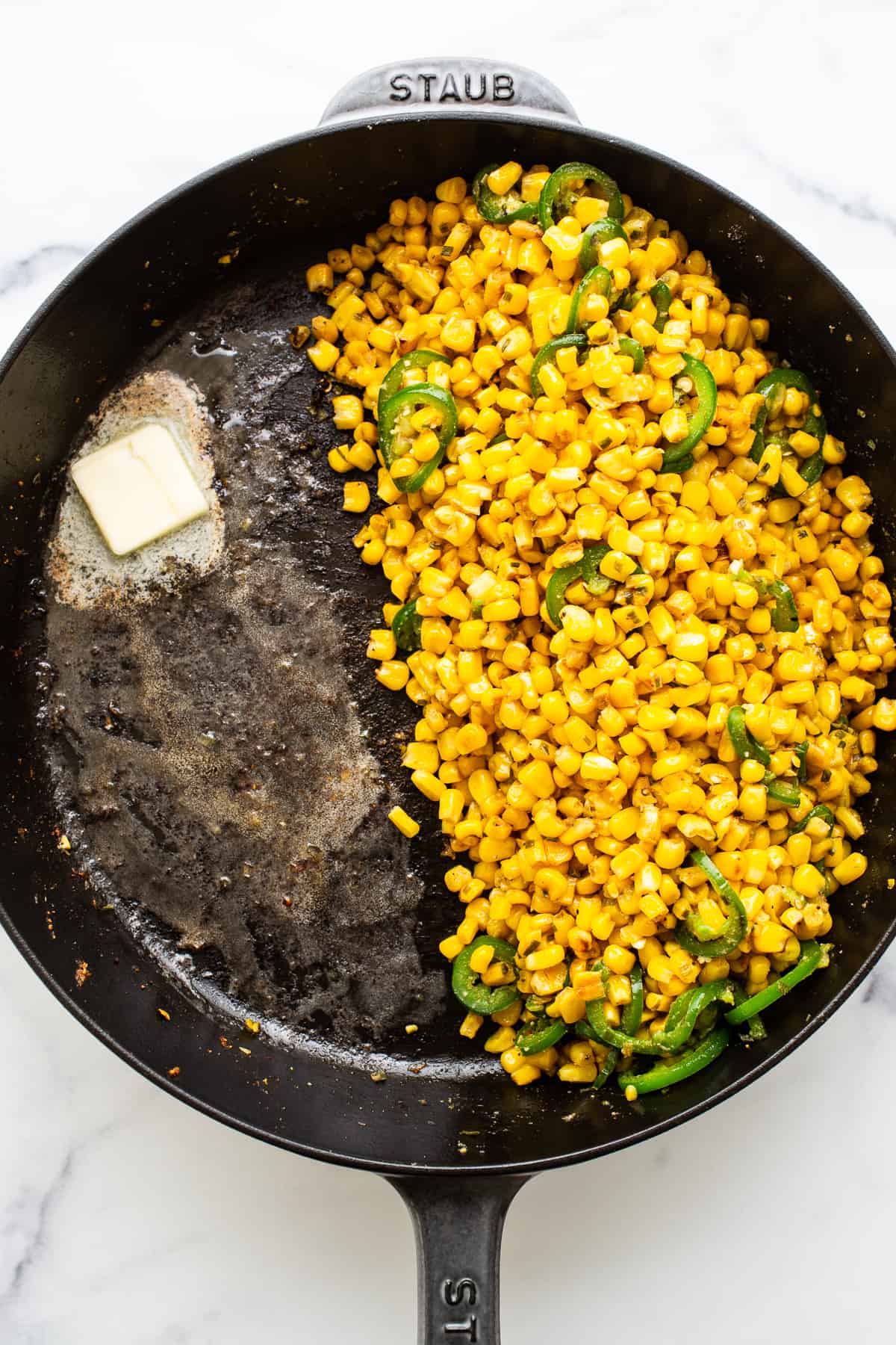 Corn and sliced jalapenos in a cast iron skillet with a pad of melting butter.
