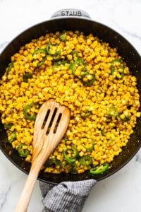 Corn and jalapenos in a skillet with a wooden spoon.