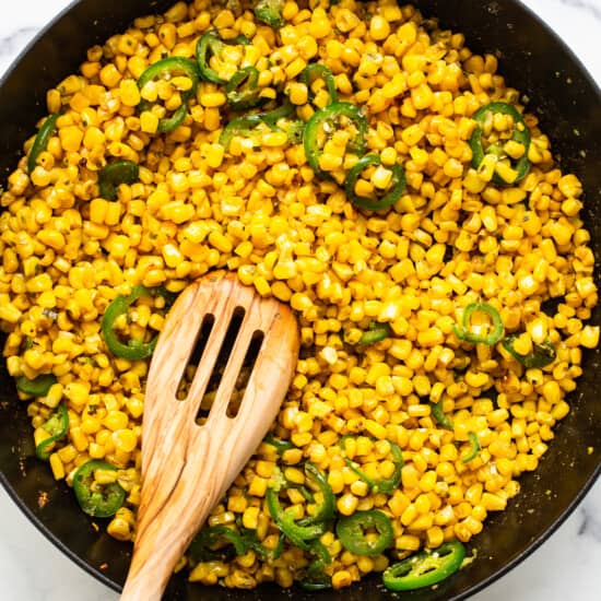 Corn and jalapenos in a skillet with a wooden spoon.