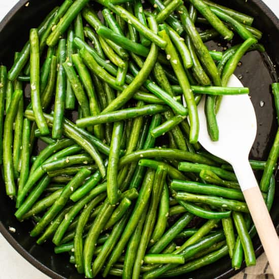 Green beans in a skillet with a wooden spoon.