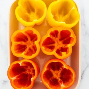 Sliced red and yellow peppers in a white baking dish.