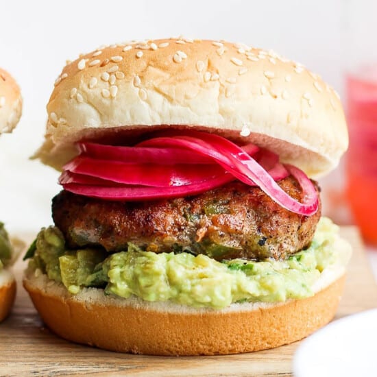 Two turkey burgers with guacamole and onions on a cutting board.