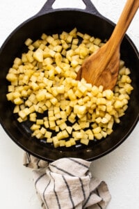 Cubed potatoes in a skillet with a wooden spoon.