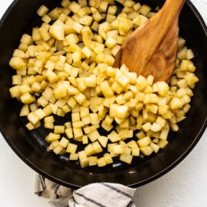 Cubed potatoes in a skillet with a wooden spoon.