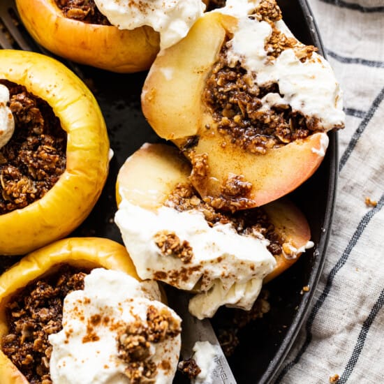Stuffed apples in a skillet with whipped cream and granola.
