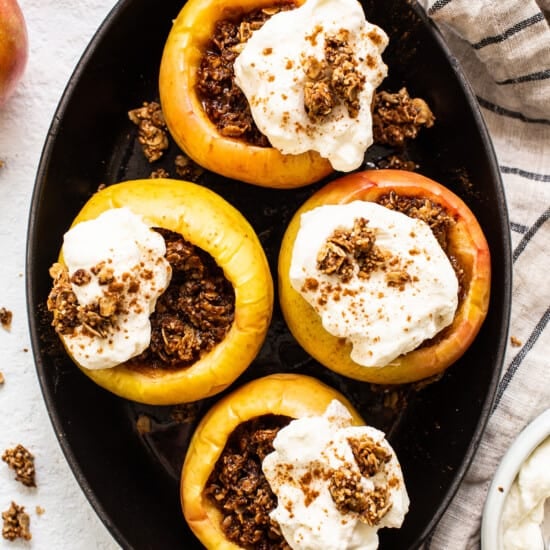 Stuffed apples in a skillet with whipped cream and granola.