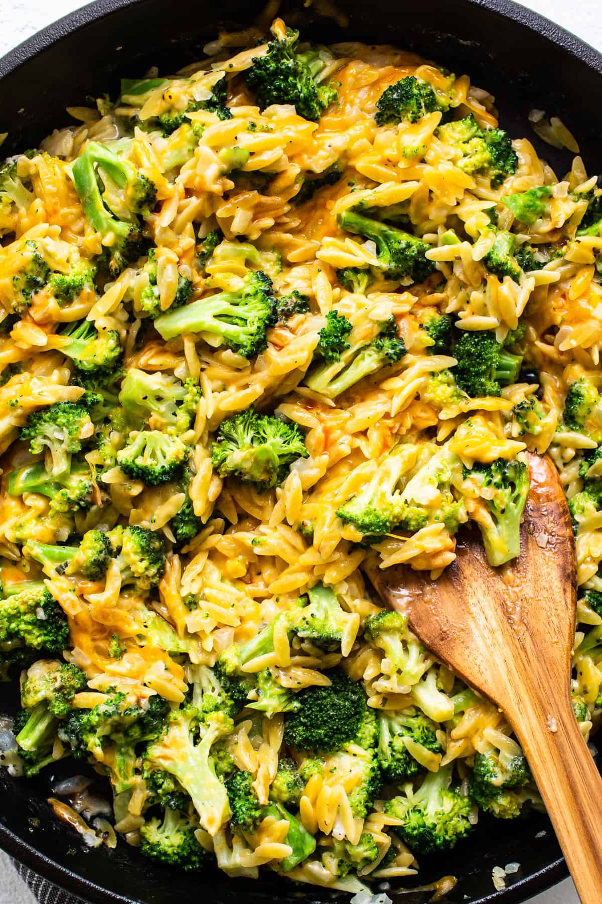 mixing broccoli and cheese with orzo in a cast iron skillet.