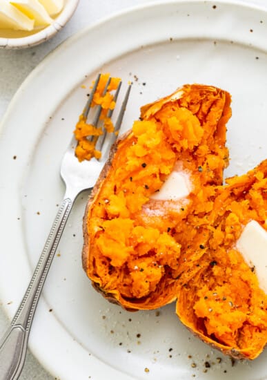 A sweet potato on a plate with a pad of butter, and salt and pepper.